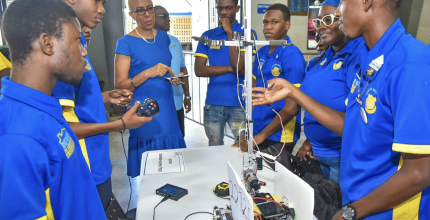 Students gathered around a robot. Photograph published by NY Carib News and Caribbean National Weekly. No photo credit was printed.